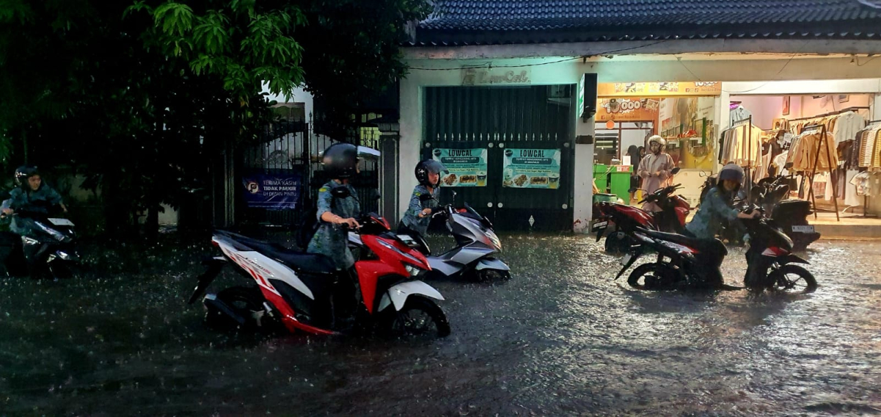 Pengendara motor yang melintas di Jalan Raya Spande Sidoarjo terpaksa menuntun motornya yang mogok akibat banjir, Rabu (19/11/2025).
